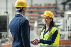 A woman shaking a man's hand and smiling in a warehouse