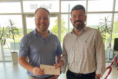 Two men smiling and holding a check in an office setting