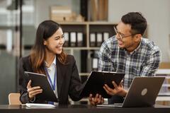 A middle-aged businessman, a young businesswoman, and Asian individuals are collaborating at desks