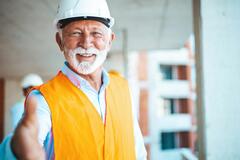 Photo of an older man in an orange safety vest smiling and holding his hand out