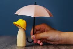 Closeup of a hand holding a toy umbrella over a wooden figure
