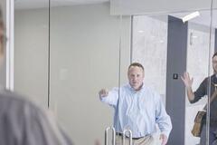 Two men greeting another man through a set of glass doors