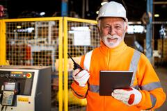 Older man in orange safety vest smiling in a factory setting