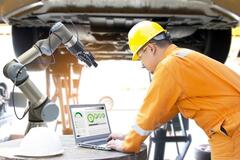 A man in a manufacturing plant using a laptop to run a machine