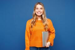 Young woman in an orange sweater smiling and holding a laptop