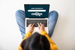 Birds-eye view of a young woman sitting on the floor with a laptop doing a job search online
