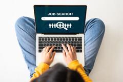 Birds-eye view of a young woman sitting on the floor with a laptop doing a job search online