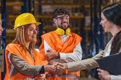 Warehouse workers in safety vests and hard hats greet a manager
