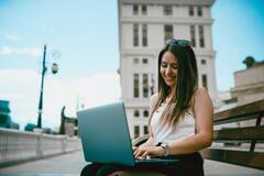Young woman smiling while using a laptop outside