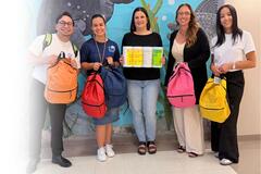 A group of Spherion professionals smiles while holding school backpacks to be donated to local students.