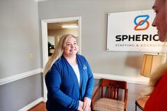 A young woman smiles at another woman in front of a Spherion Staffing sign inside a Spherion office