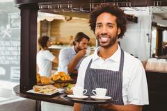 Server, young man smiling serving tray of coffee