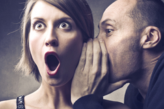 A man telling a shocked woman a secret