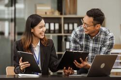 A middle-aged businessman, a young businesswoman, and Asian individuals are collaborating at desks