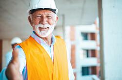 Photo of an older man in an orange safety vest smiling and holding his hand out