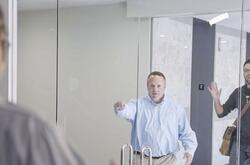 Two men greeting another man through a set of glass doors