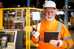 Older man in orange safety vest smiling in a factory setting