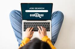 Birds-eye view of a young woman sitting on the floor with a laptop doing a job search online