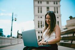 Young woman smiling while using a laptop outside