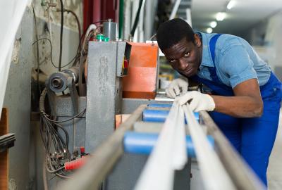 A man in a blue apron focuses on measuring a metal beam