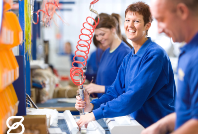 A woman in a blue suit smiles as she works on a product assembly line.