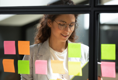 A woman looks over her organized sticky notes on a window as part of her project management