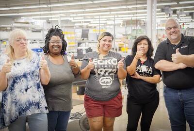 Four printing employees smiling at the camera and giving a thumbs up