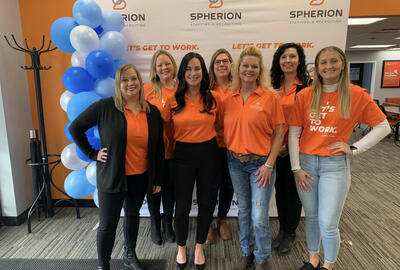A group of women in orange shirts smiling and posing in an office setting