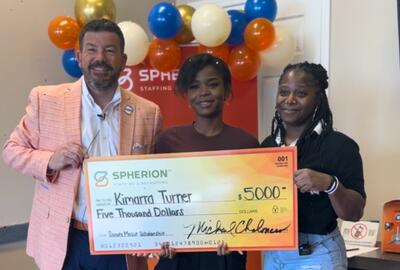 Three people smiling and holding a giant orange check