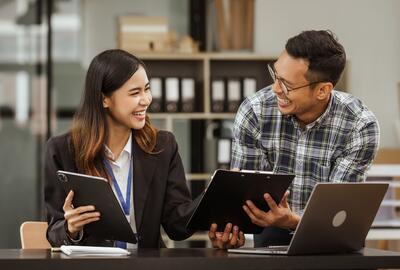 A middle-aged businessman, a young businesswoman, and Asian individuals are collaborating at desks