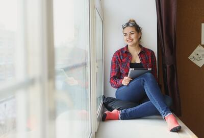 Young woman holding a tablet and looking out the window