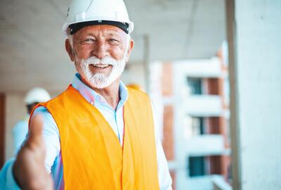 Photo of an older man in an orange safety vest smiling and holding his hand out