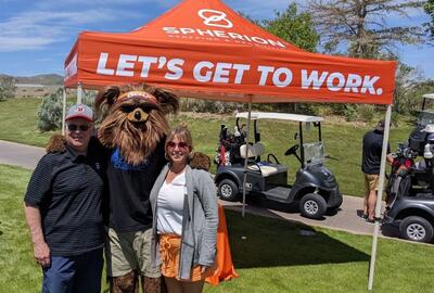 A man and a woman with a bear mascot posing on a golf course
