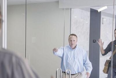 Two men greeting another man through a set of glass doors
