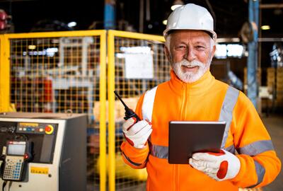 Older man in orange safety vest smiling in a factory setting