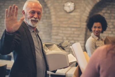 An older man waving goodbye to the camera while smiling