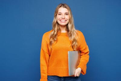 Young woman in an orange sweater smiling and holding a laptop