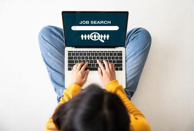 Birds-eye view of a young woman sitting on the floor with a laptop doing a job search online