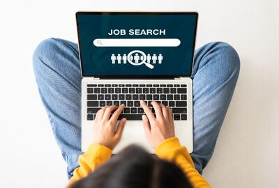 Birds-eye view of a young woman sitting on the floor with a laptop doing a job search online