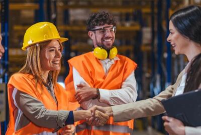Warehouse workers in safety vests and hard hats greet a manager