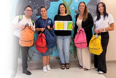 A group of Spherion professionals smiles while holding school backpacks to be donated to local students.
