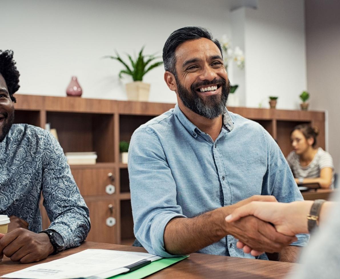 Man in an office smiling and shaking hands with someone off camera