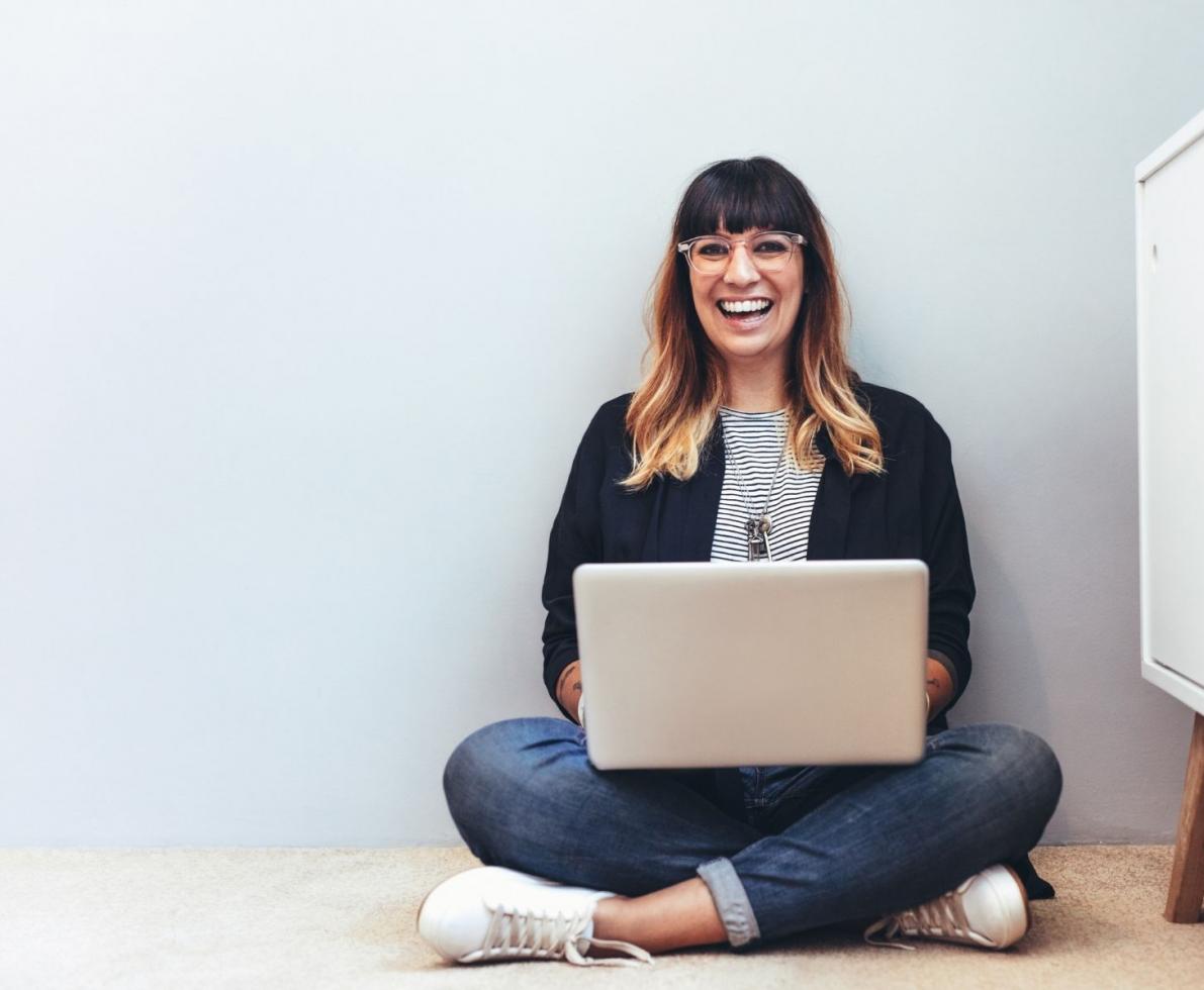 Woman sitting corss-legged on the floor with a laptop in her lap