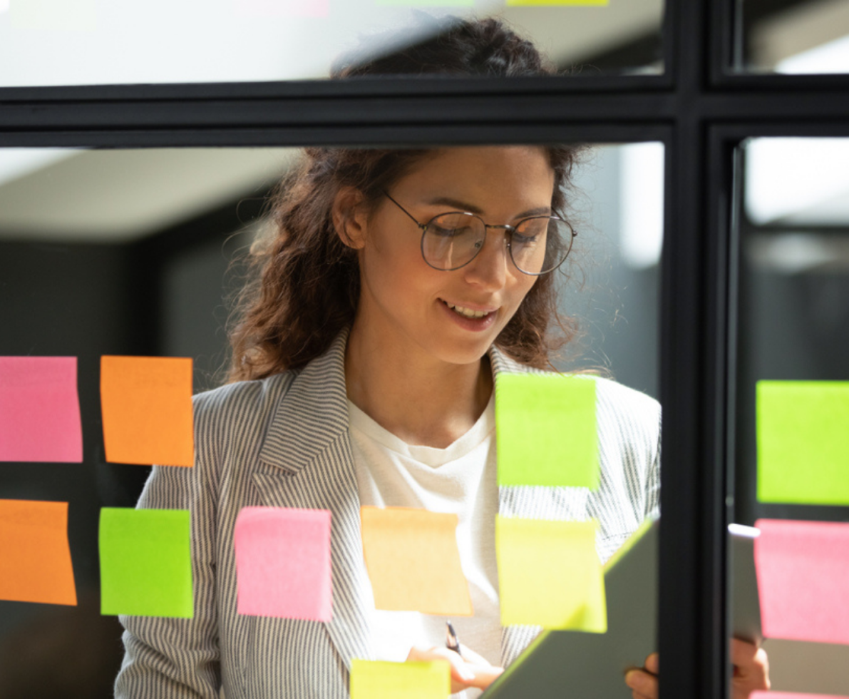 A woman looks over her organized sticky notes on a window as part of her project management