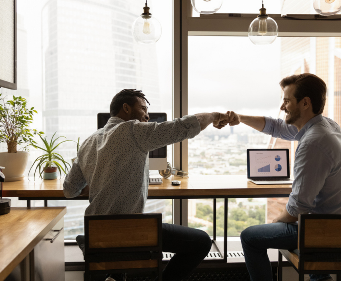 Two men fist bumping and celebrating their work success in a dim office setting