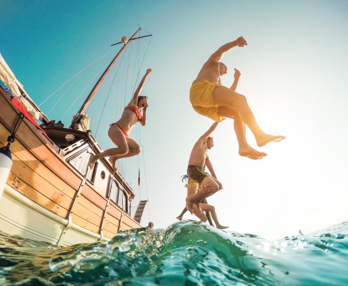 Happy friends jumping from a boat into the sea