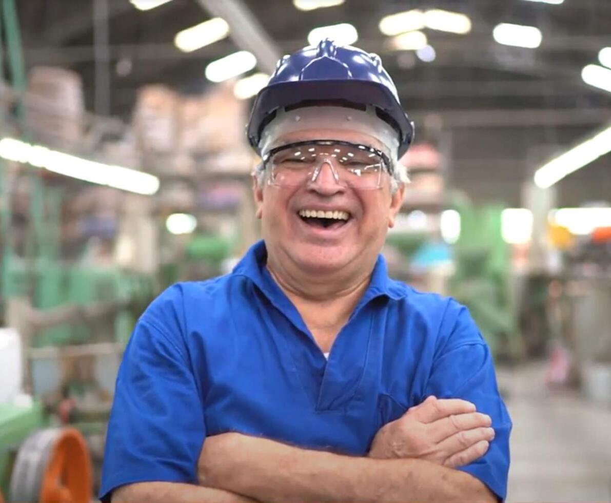 Older man in blue hard hat laughing at the camera