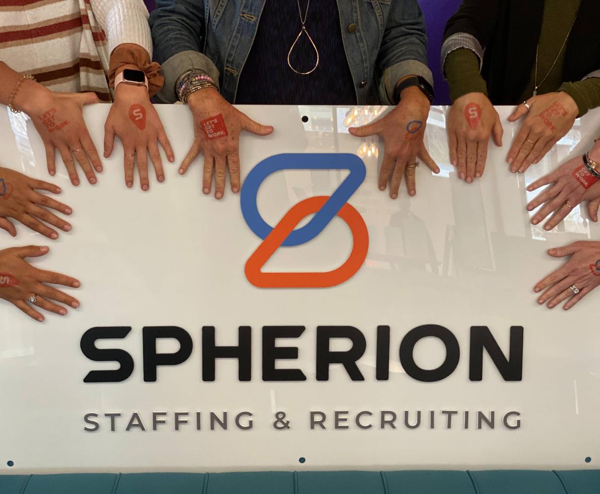 Hands surrounding a white Spherion logo sign