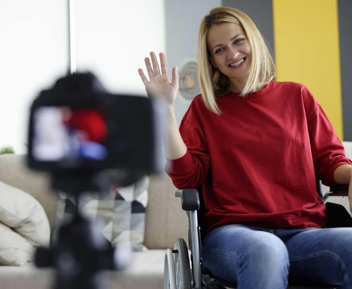 Sales_representative_-_Woman_in_red_sweater_sitting_in_a_wheelchair_waving_at_a_camera