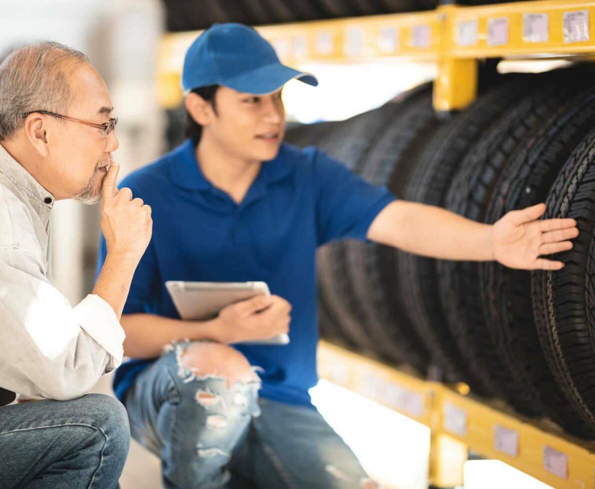 Sales_representative_-_Young_Asian_man_showing_an_older_customer_a_row_of_tires